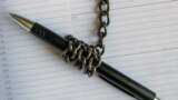 A pen wrapped in an iron chain lies on an empty notebook. Concept- restriction of freedom of speech.