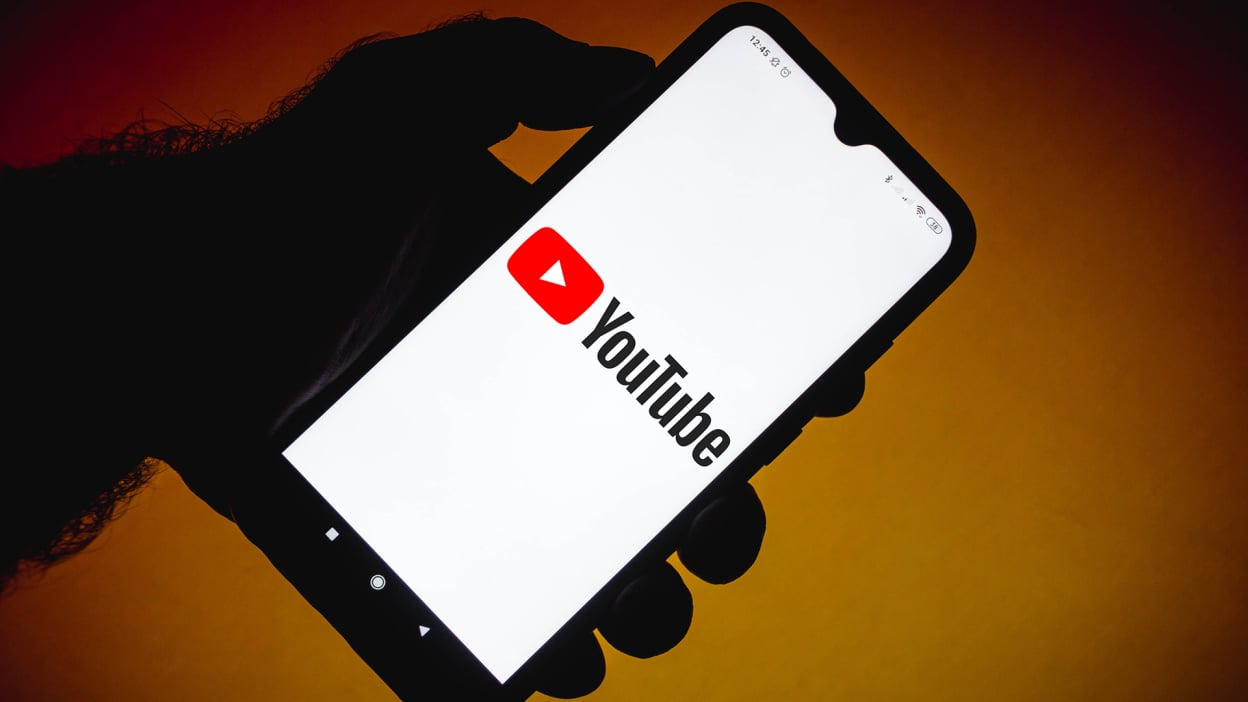 Hand holding a smartphone with the YouTube logo on screen.
