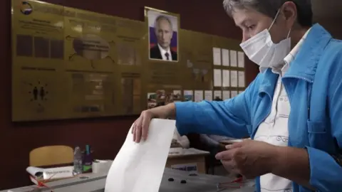 EPA A woman voting in Russia's constitutional referendum under a poster of Vladimir Putin, June 2020