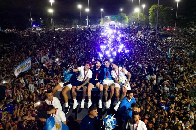 Argentina's captain and forward Lionel Messi (C) holds the FIFA World Cup Trophy on board a bus as he celebrates alongside teammates and supporters (AFP via Getty Images)