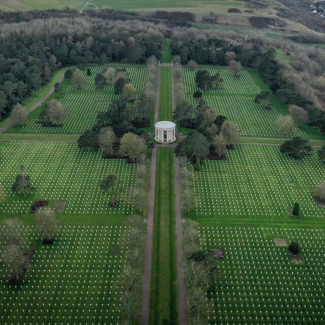 An aerial view of a vast cemetery surrounded by trees. A round white structure is in the middle of the cemetery.
