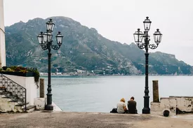 Rear View Of People Sitting By Antique Street Light In Atrani, Italy